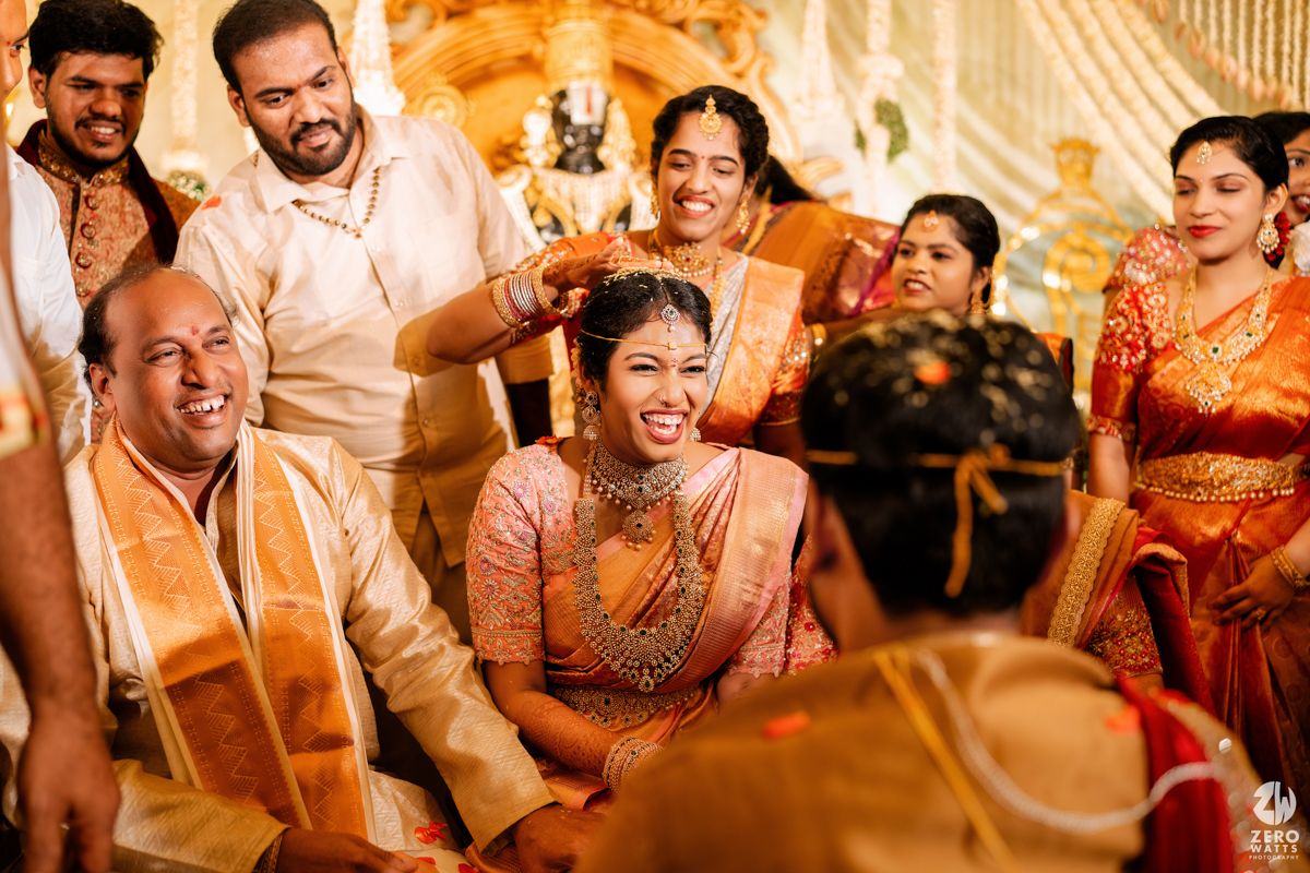 Candid moment of laughter during South Indian wedding ceremony with traditional decorations.