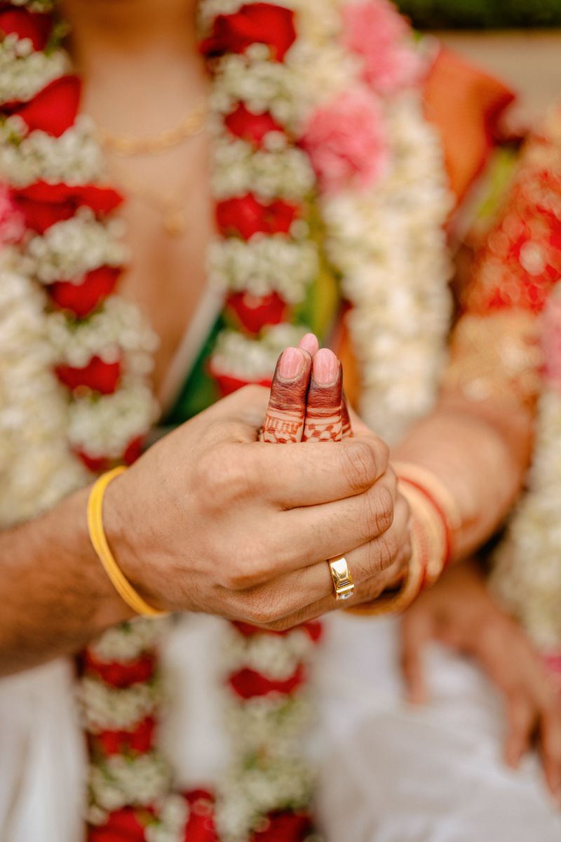 Close-up of hands wearing wedding rings and jasmine flower garlands during a traditional Indian marriage ceremony.