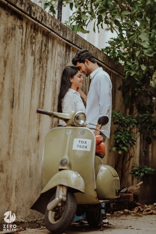 Couple posing with vintage Vespa scooter against weathered wall.