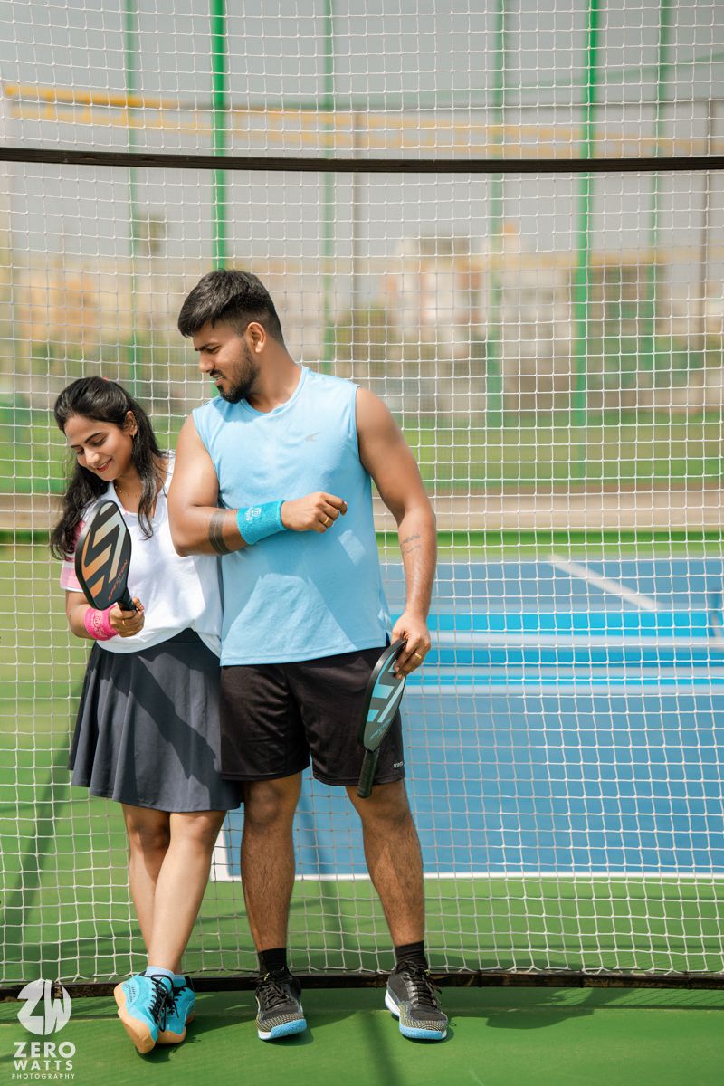 People in sportswear interacting on a tennis court with green fence backdrop.