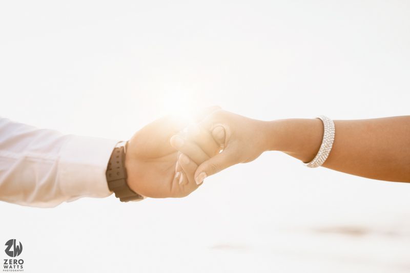Close-up of two hands reaching out to hold each other against a bright sunlit background.