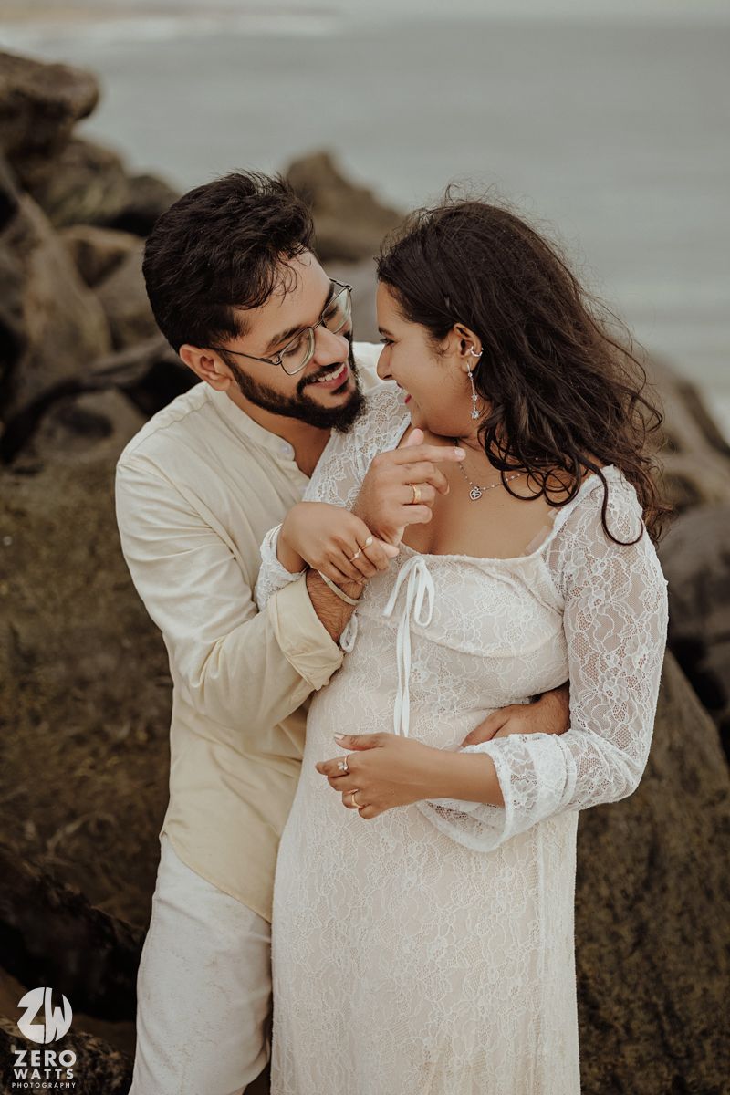 An intimate couple shares a tender moment on a rocky beach during a photoshoot.