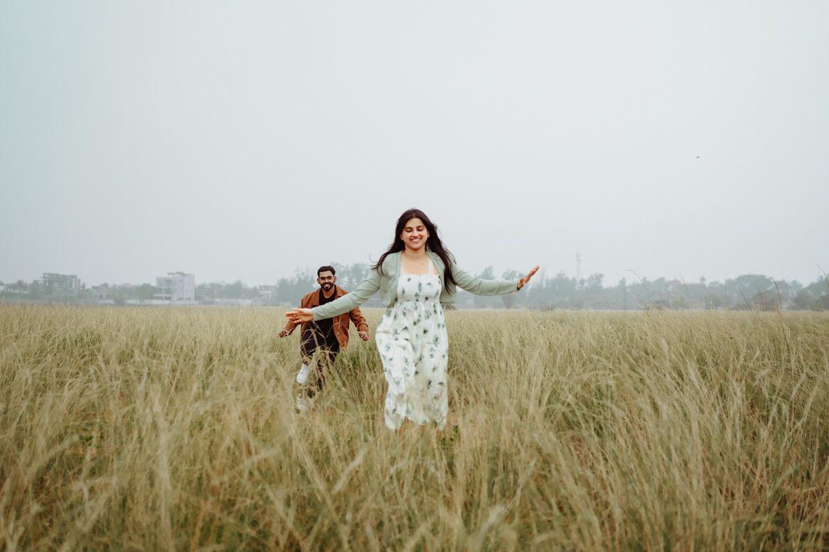 A couple stands joyfully in a tall grass meadow on an overcast day.