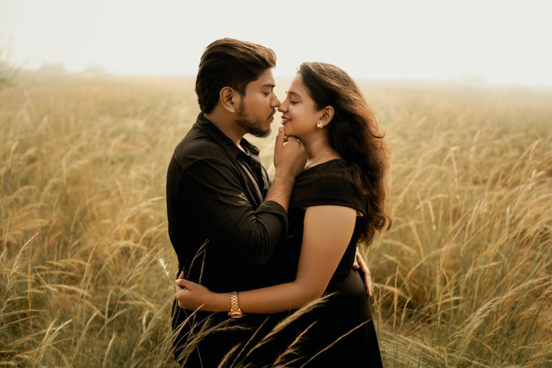 Romantic couple embraces in golden wheat field during sunset with warm moody lighting.