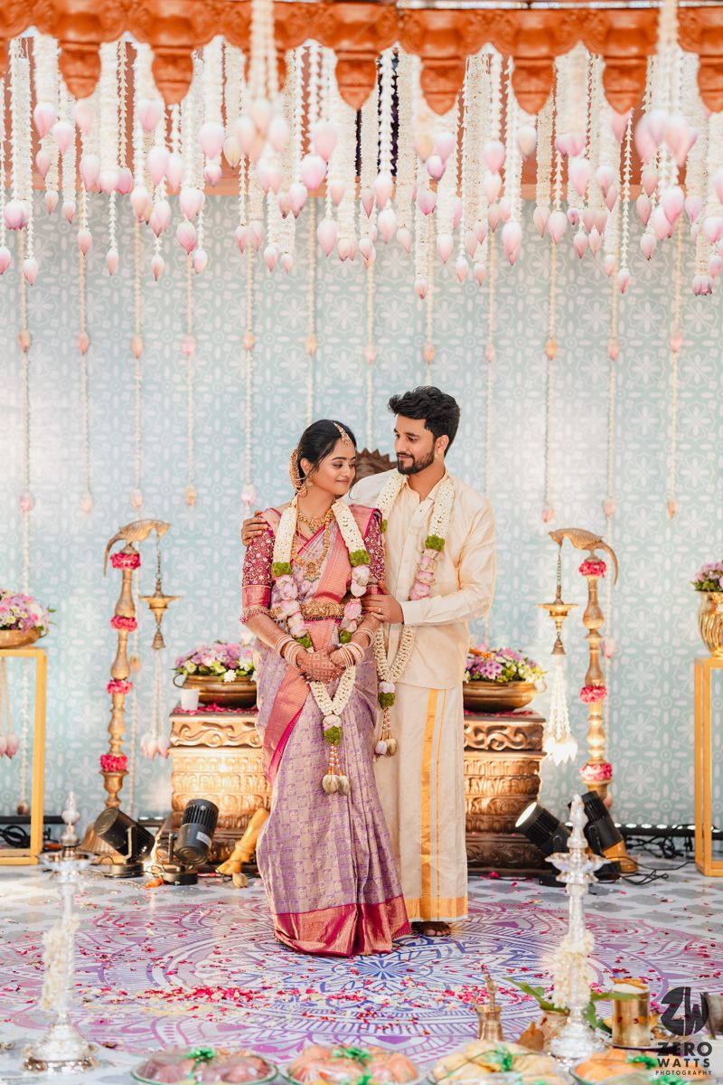 Wedding ceremony under hanging floral decor with couple in traditional South Indian attire.