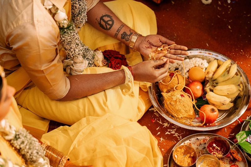 Traditional Indian wedding ritual showing hands exchanging food during ceremony with yellow and gold decor.