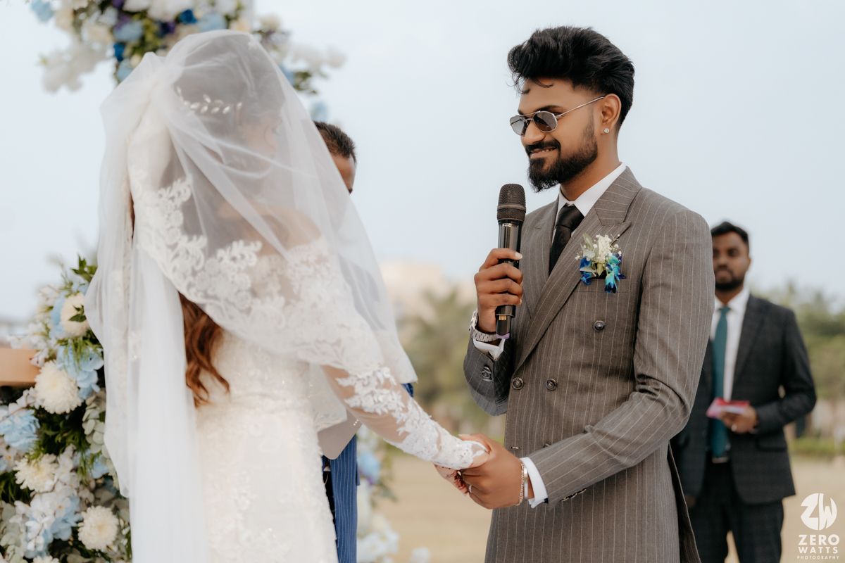 A couple shares a moment during their wedding ceremony as the groom speaks into a microphone while holding hands.