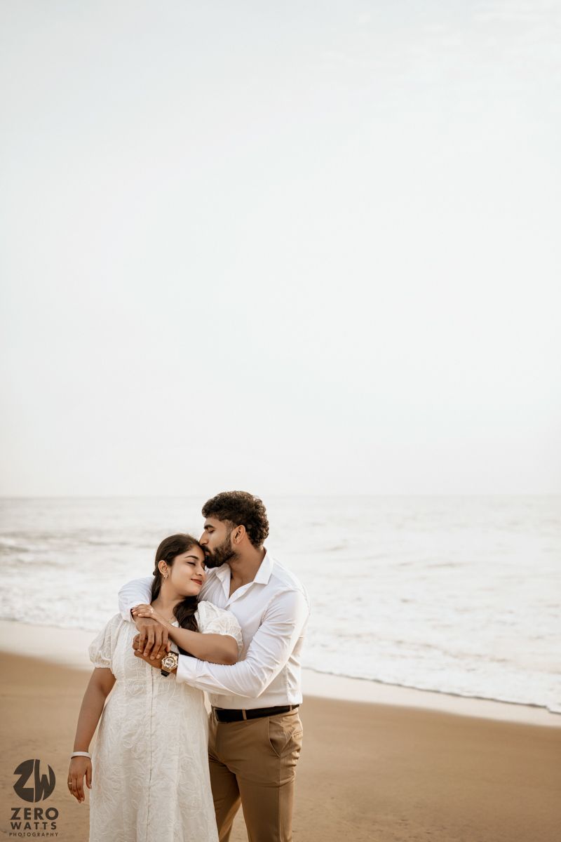 A romantic beachside portrait session with two people in white outfits sharing an intimate moment.