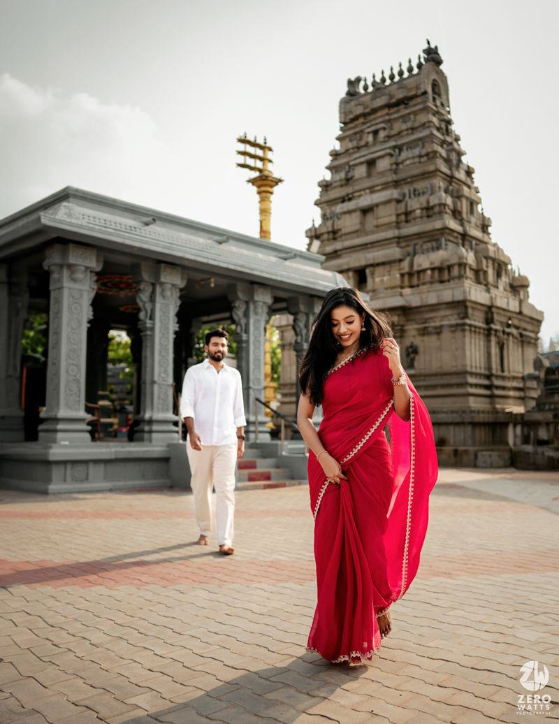 A couple poses at a Hindu temple complex with traditional architecture and pillared mandapa in the background.