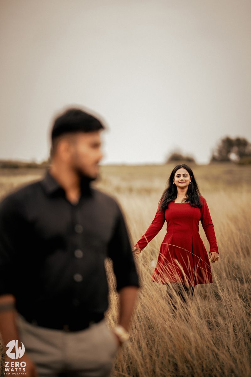 Couple in red and black attire walking through a rustic field.