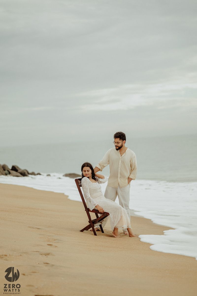Romantic beach photoshoot featuring a wooden chair and gentle waves on an overcast day.