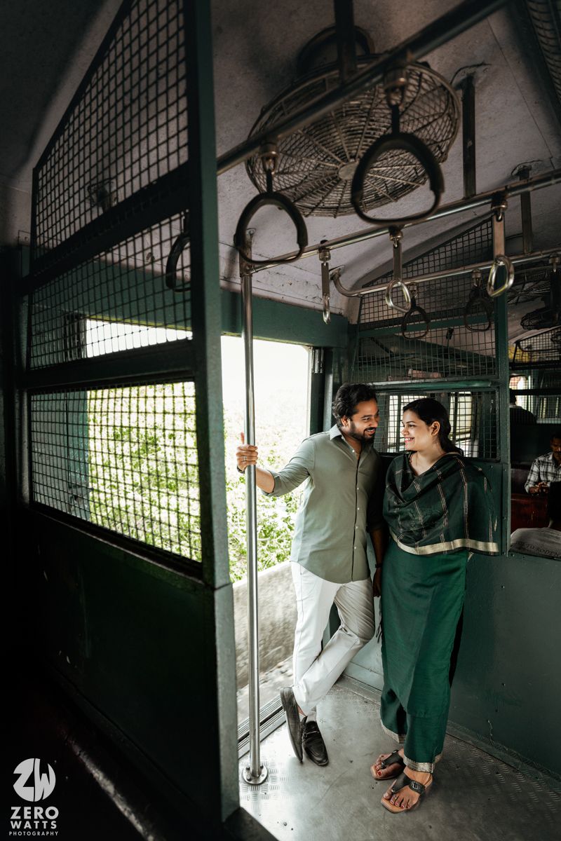 Two people standing in a train corridor with sunlight filtering through metal mesh windows.
