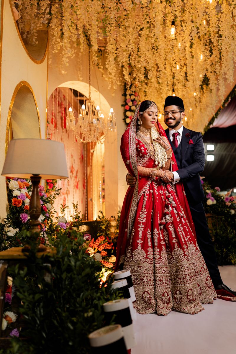 Elegant wedding portrait against golden floral backdrop with traditional South Asian attire.
