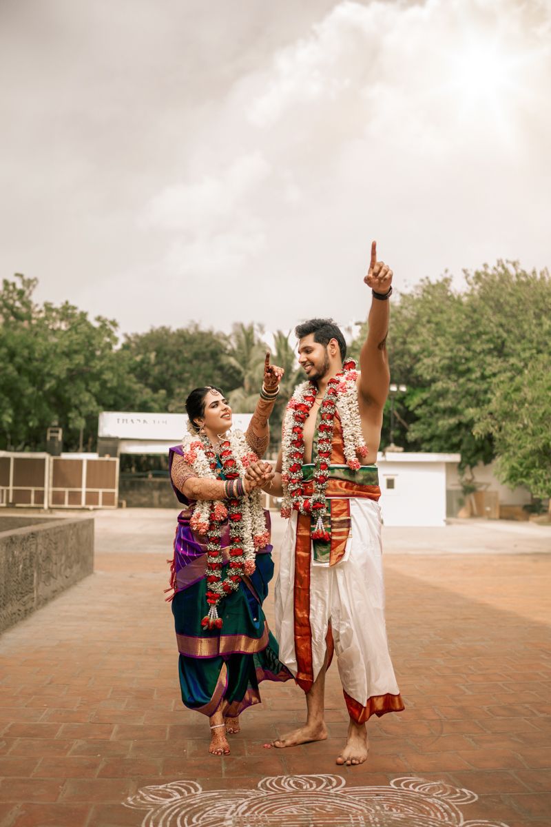 Couple in traditional South Indian attire performing a joyful dance ritual with decorative kolam design on floor.