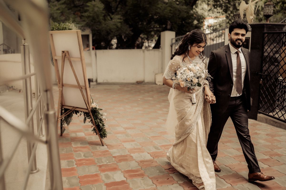 A couple walks together on a patterned tile courtyard, with the bride holding a bouquet in her white dress.