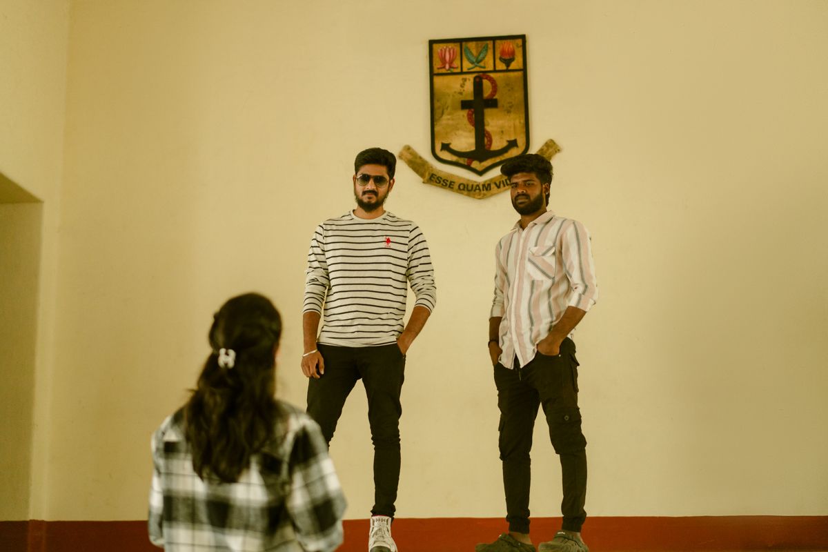 Three people standing against a beige wall with a decorative crest mounted above them.