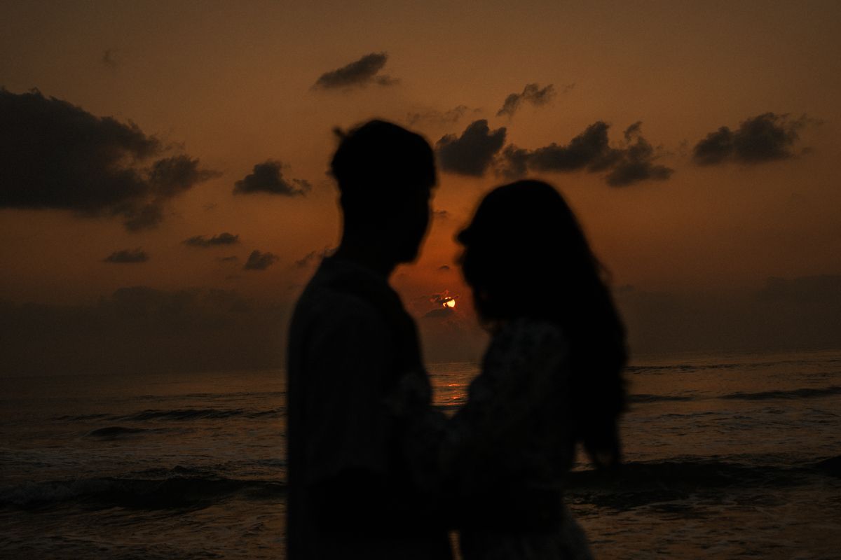 Silhouette of couple embracing during golden sunset at beach.