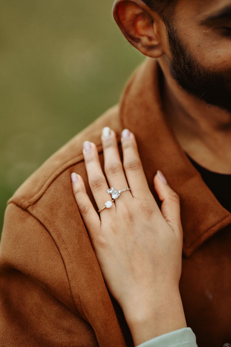 Close-up shot of a hand wearing an engagement ring resting on a brown suede jacket.