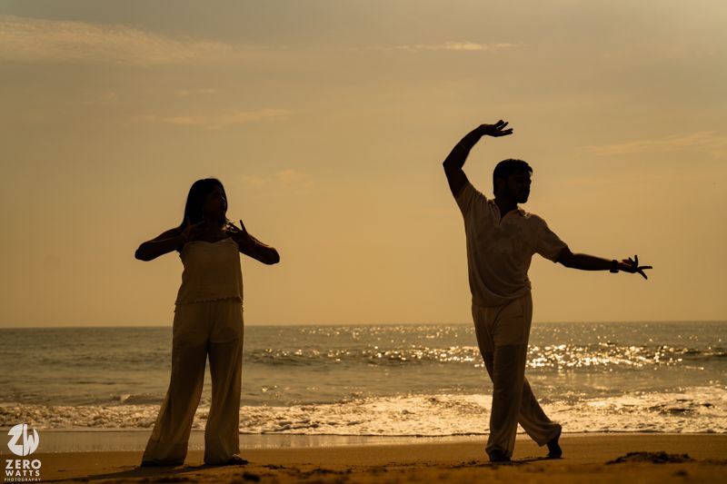 Silhouettes of people dancing and playing on a beach during golden sunset hour.