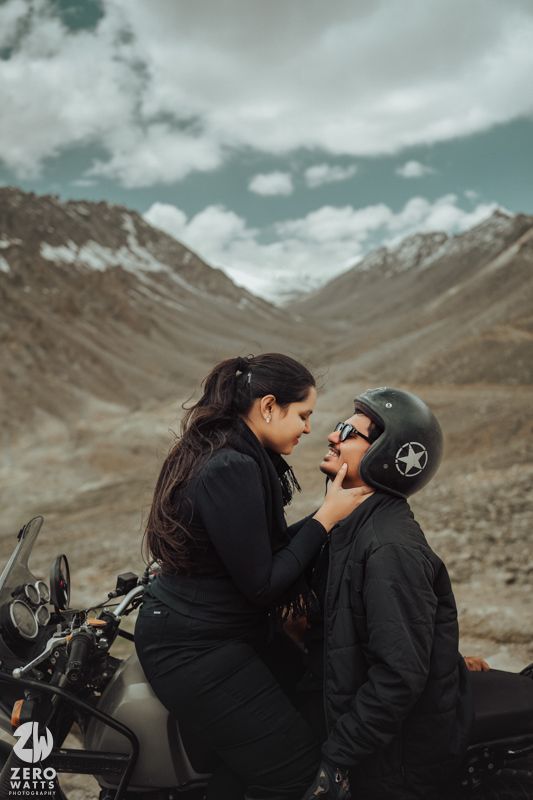 Motorcycling couple in black outfits sharing a moment in mountain landscape.