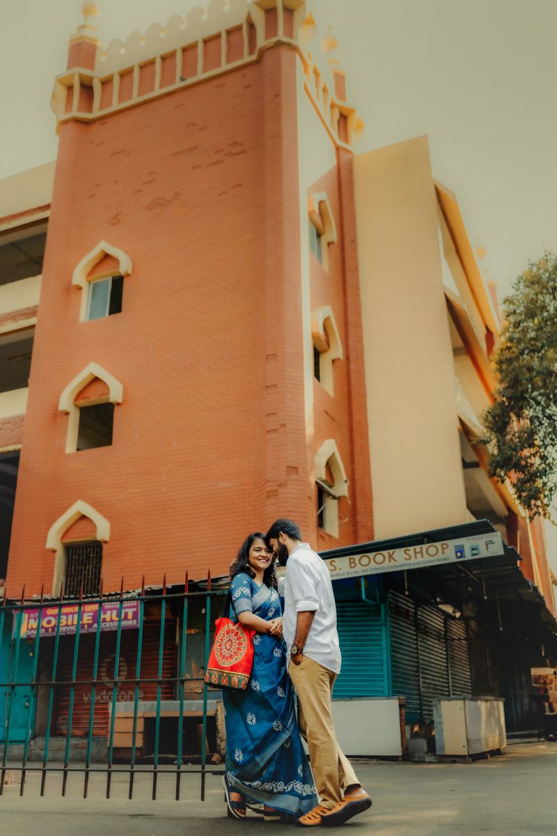 A couple stands together outside a pink tower building with gothic-style windows and architectural details.