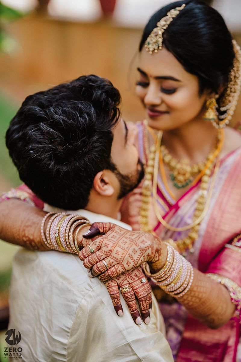Intimate wedding portrait showing bride's intricate mehndi and gold jewelry as couple shares a tender moment.