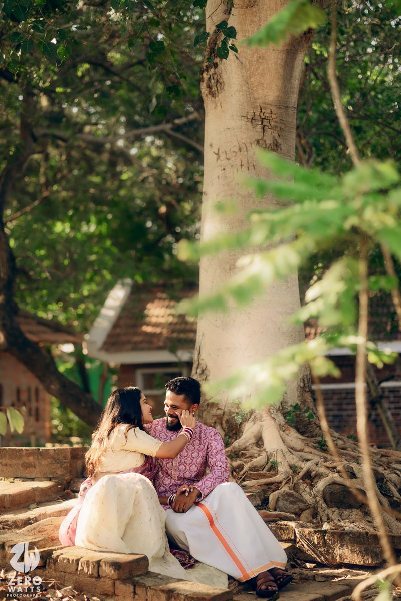 Couple in traditional Indian wear share a tender moment under a large tree.