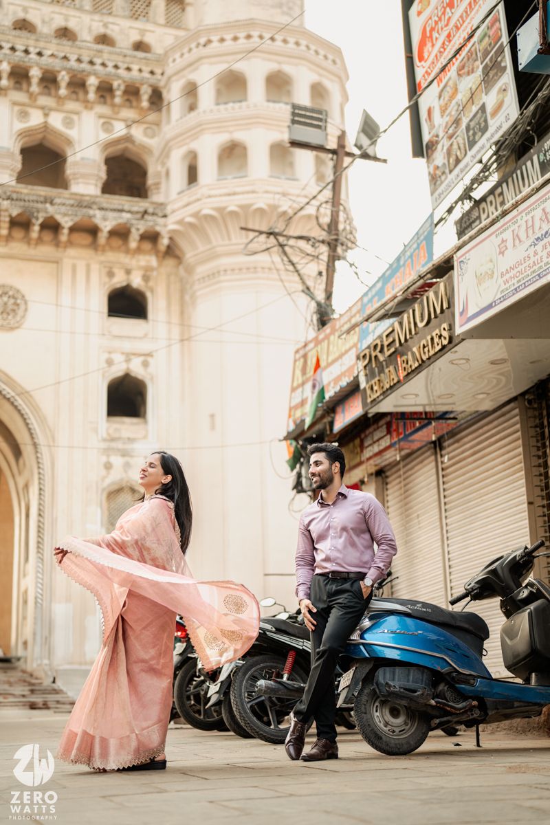 A stylish couple posing near historic architecture with parked scooters in the background.