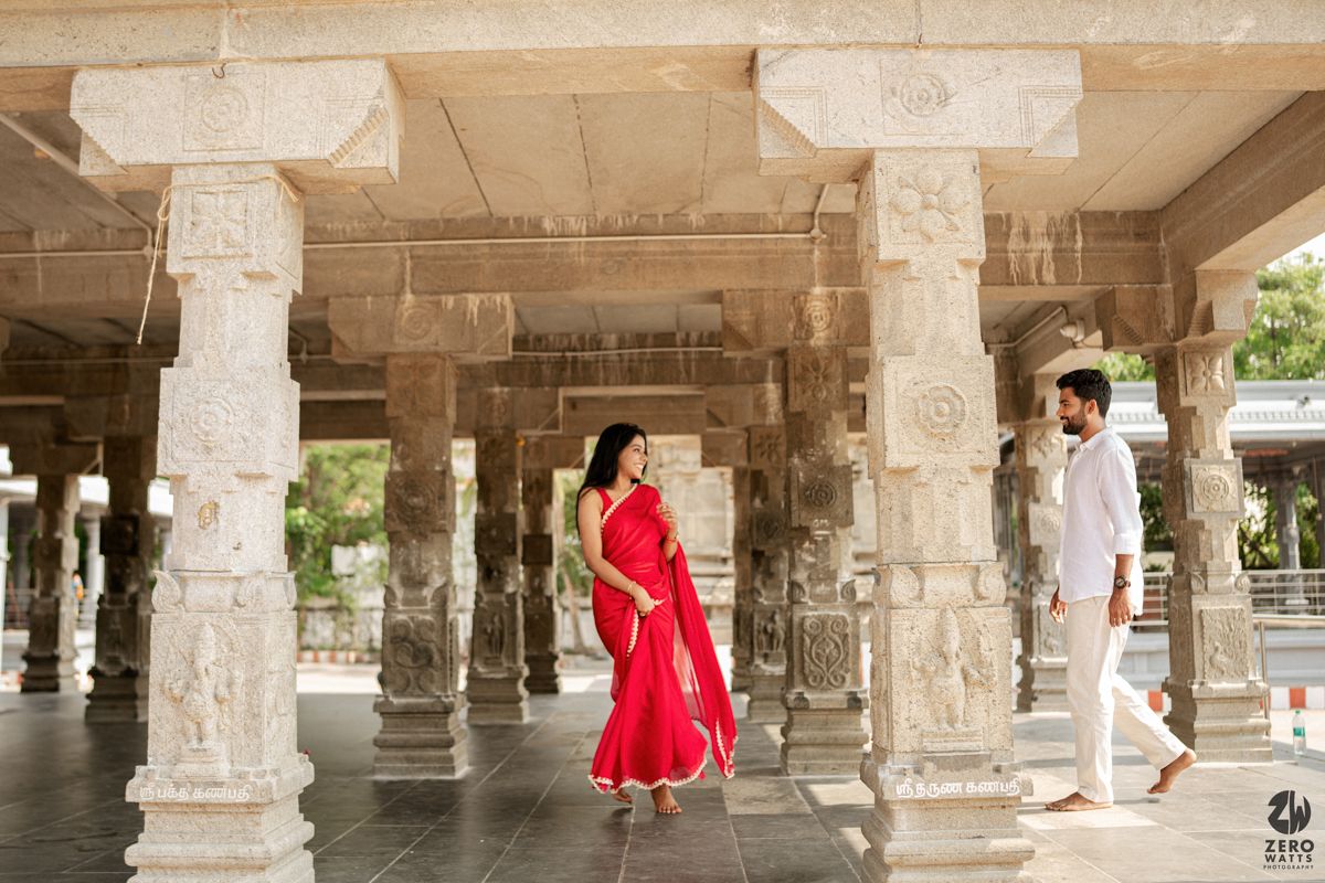 A couple in traditional attire poses amid ornate stone pillars in a historic Indian temple corridor.