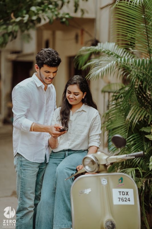 A couple sharing a lighthearted moment next to a vintage scooter surrounded by tropical plants.