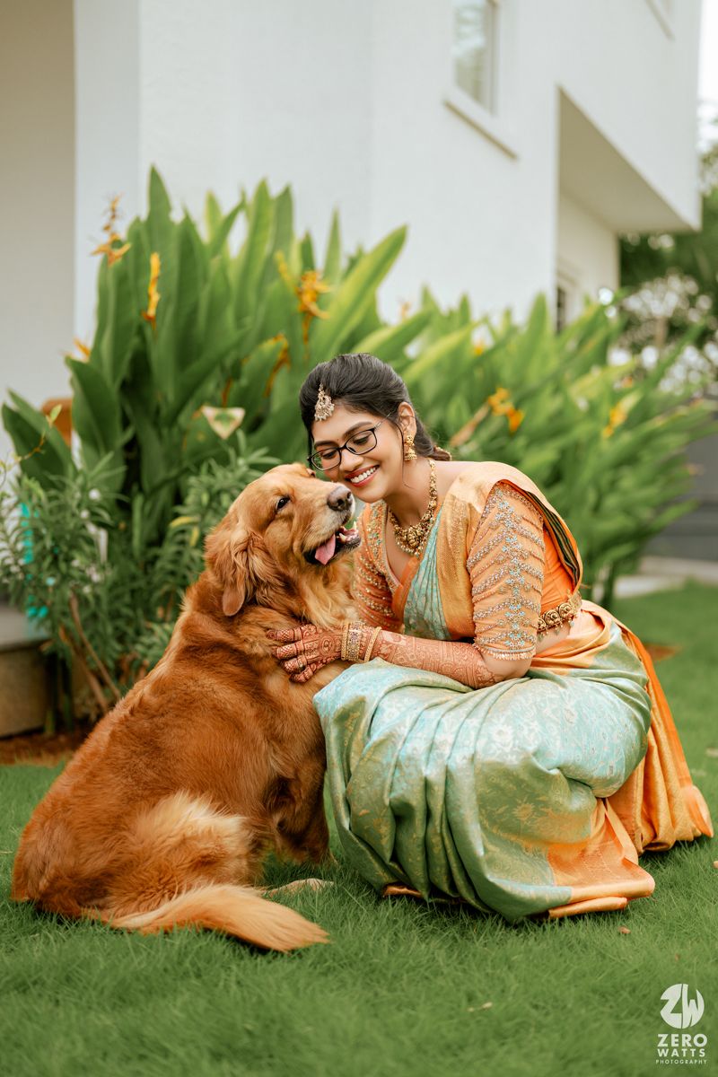 A Golden Retriever shares an affectionate moment with someone wearing traditional Indian attire on a green lawn.