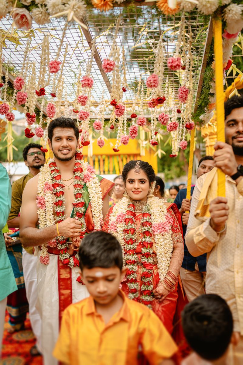 Traditional South Indian wedding ceremony with floral decorations and garlands hanging from an ornate mandap ceiling.
