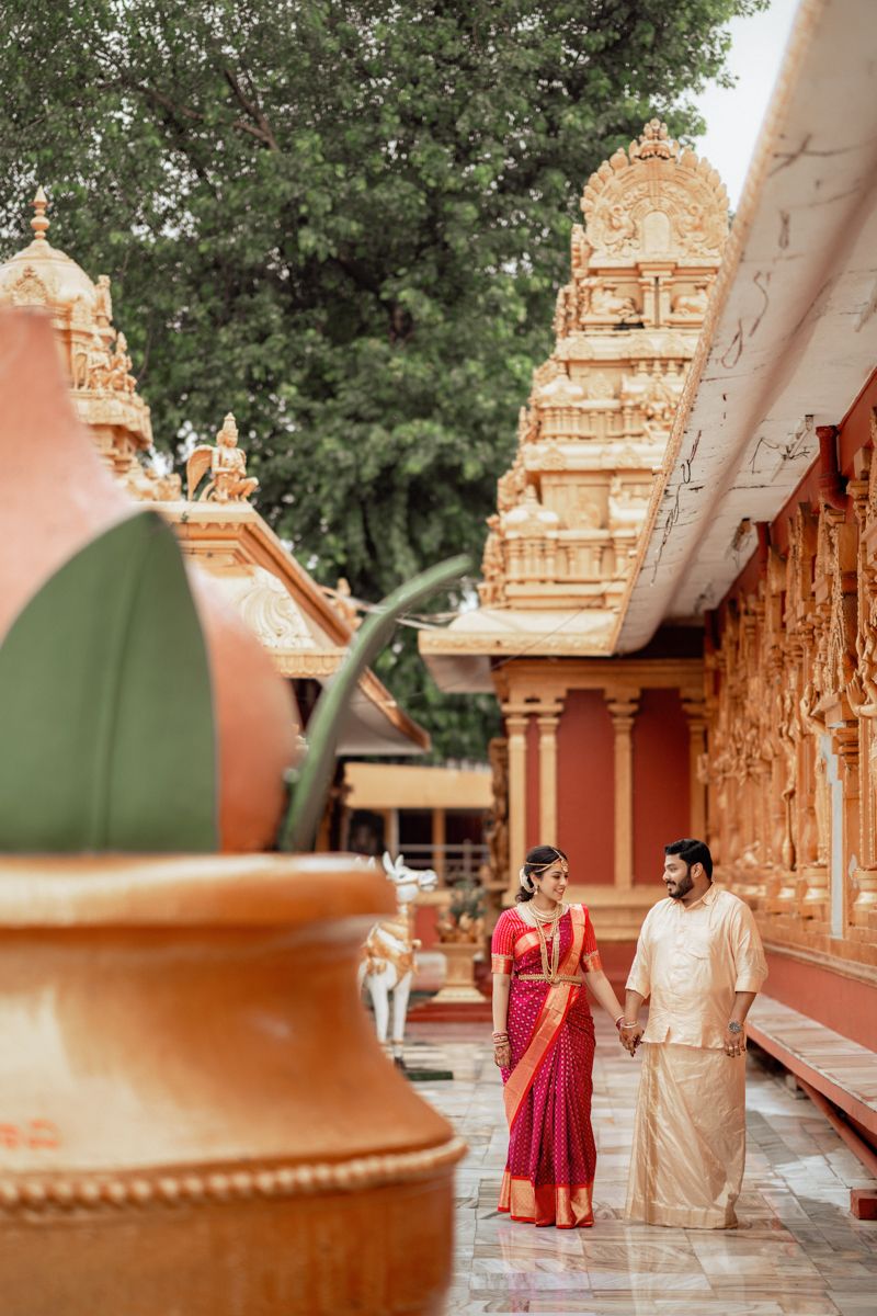 Couple in traditional dress walking along temple corridor with ornate architecture and greenery.
