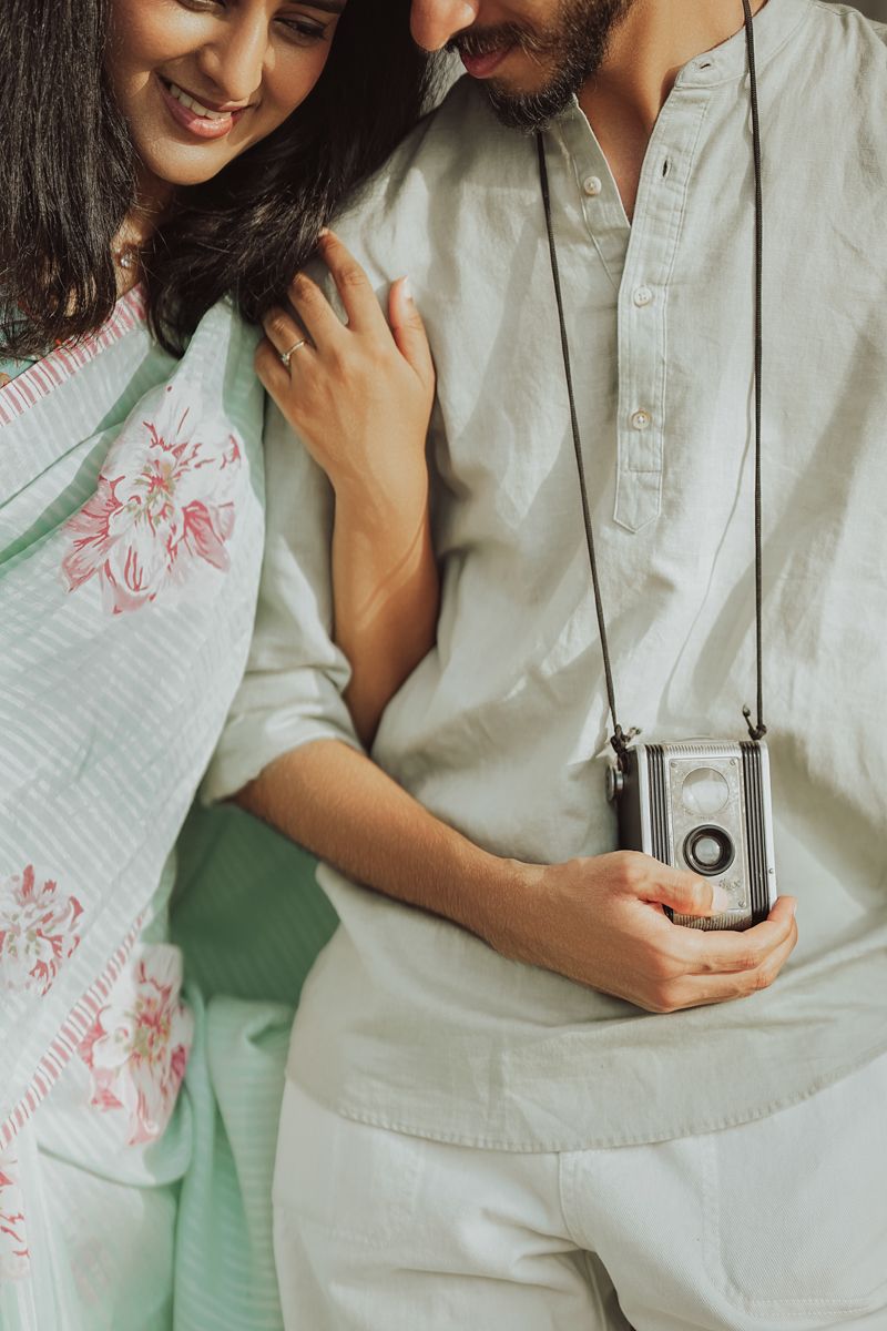 Close-up shot of couple sharing a vintage camera, wearing light colored traditional clothing with floral designs.