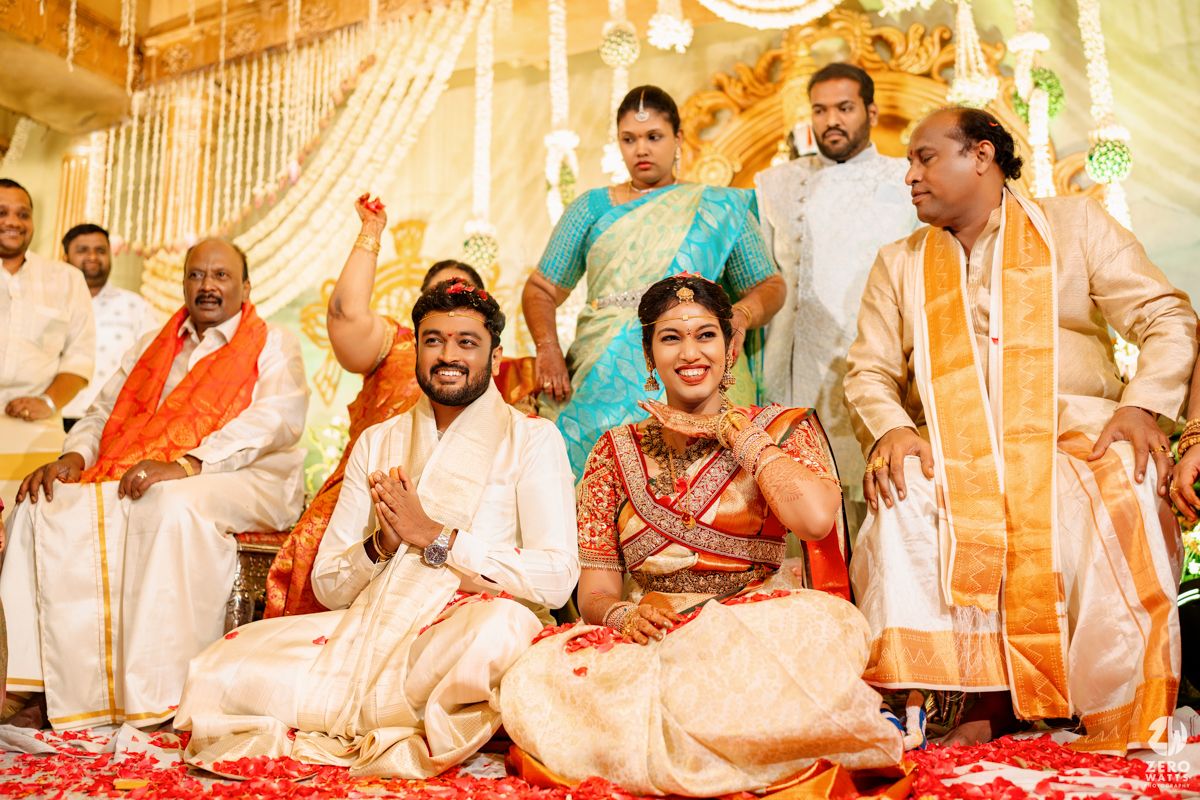 A traditional Indian wedding ceremony with celebrants seated in traditional attire amid festive decorations and flowers.