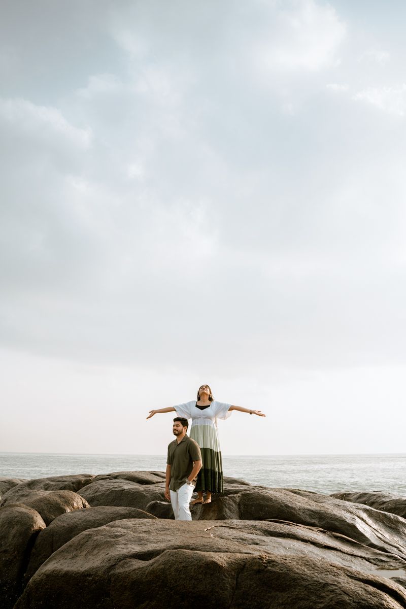 Couple standing on rocky coastal formation against cloudy sky and ocean.