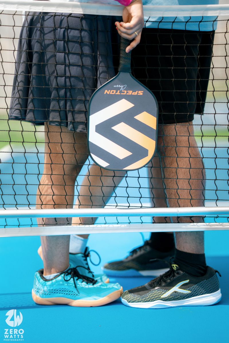 Pickleball player holds Selkirk paddle with blue sport court and net visible below.