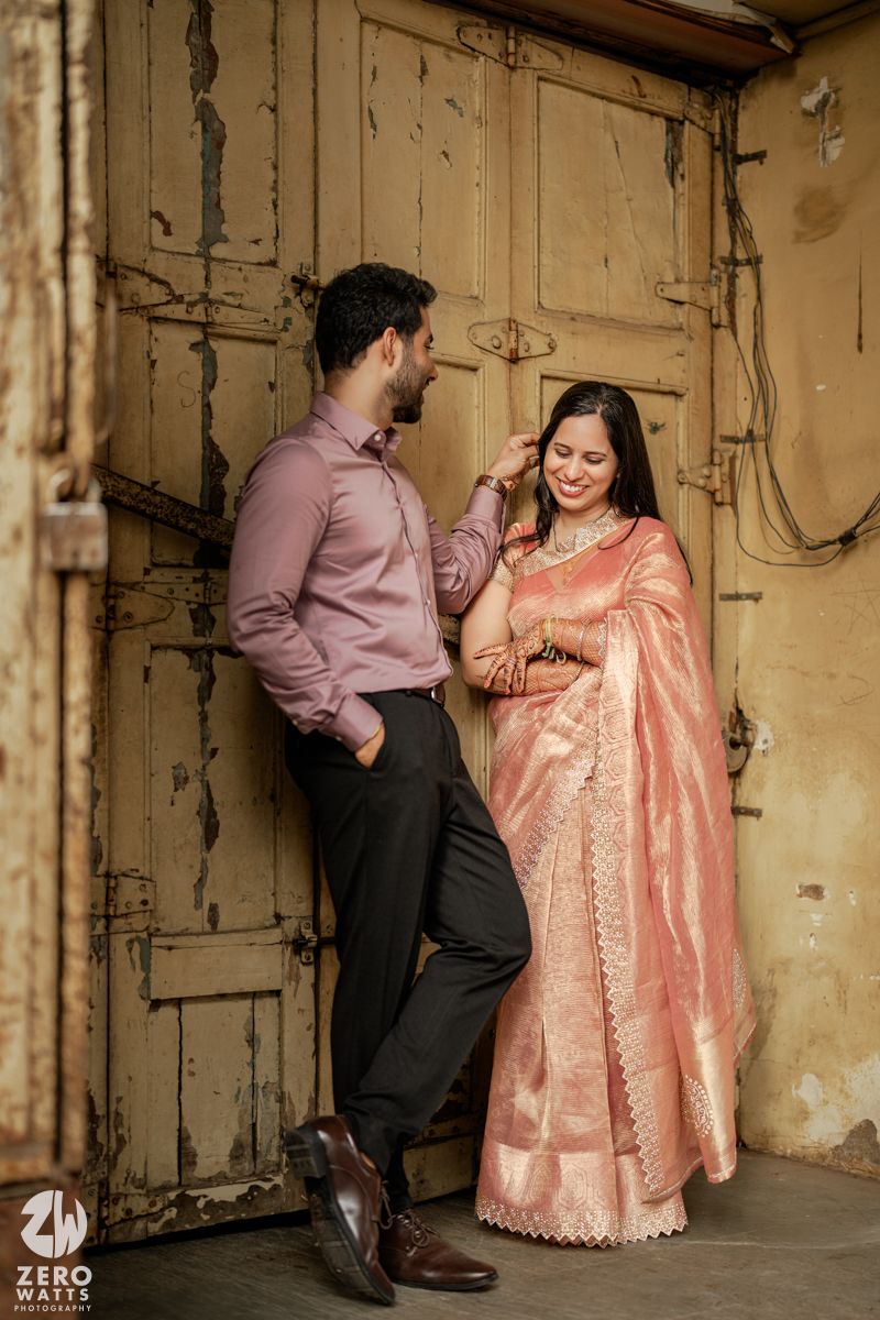 A romantic couple poses against a vintage beige door wearing formal traditional attire.
