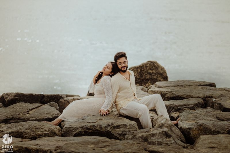 A couple lounges on rocky coastal formations during an atmospheric photoshoot.