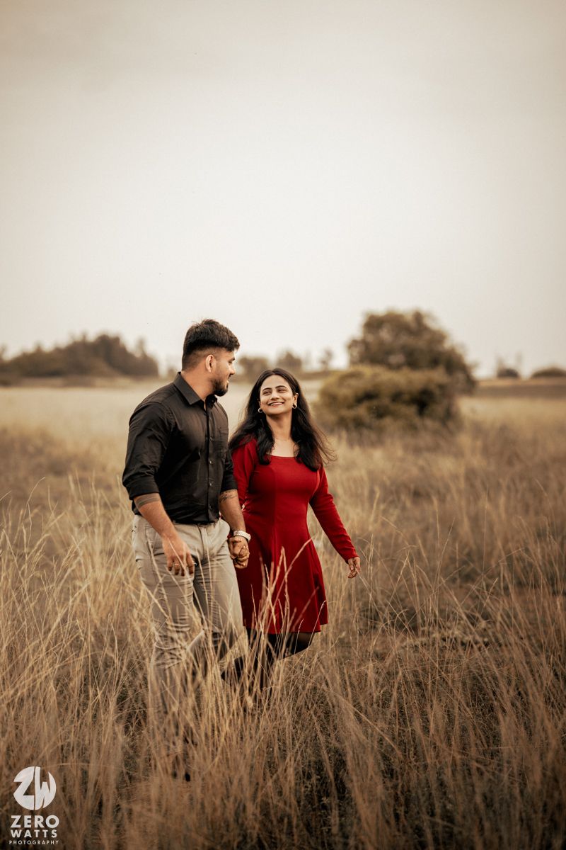 Romantic couple walking through tall grass during golden hour.