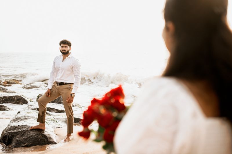 Two people share an intimate moment by the ocean shore with a bouquet of red roses.