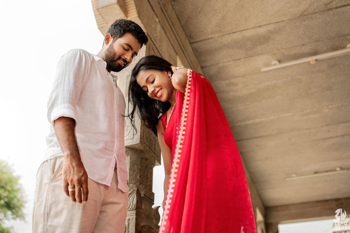 A couple in a romantic embrace outdoors, wearing contrasting white and red traditional outfits.