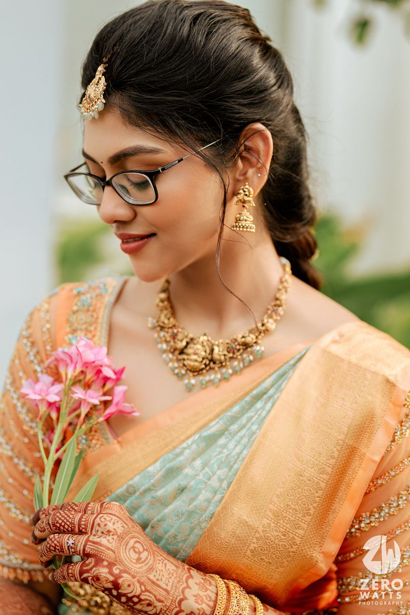 Traditional bridal portrait featuring intricate mehndi, gold jewelry and a peach silk saree with delicate pink flowers.