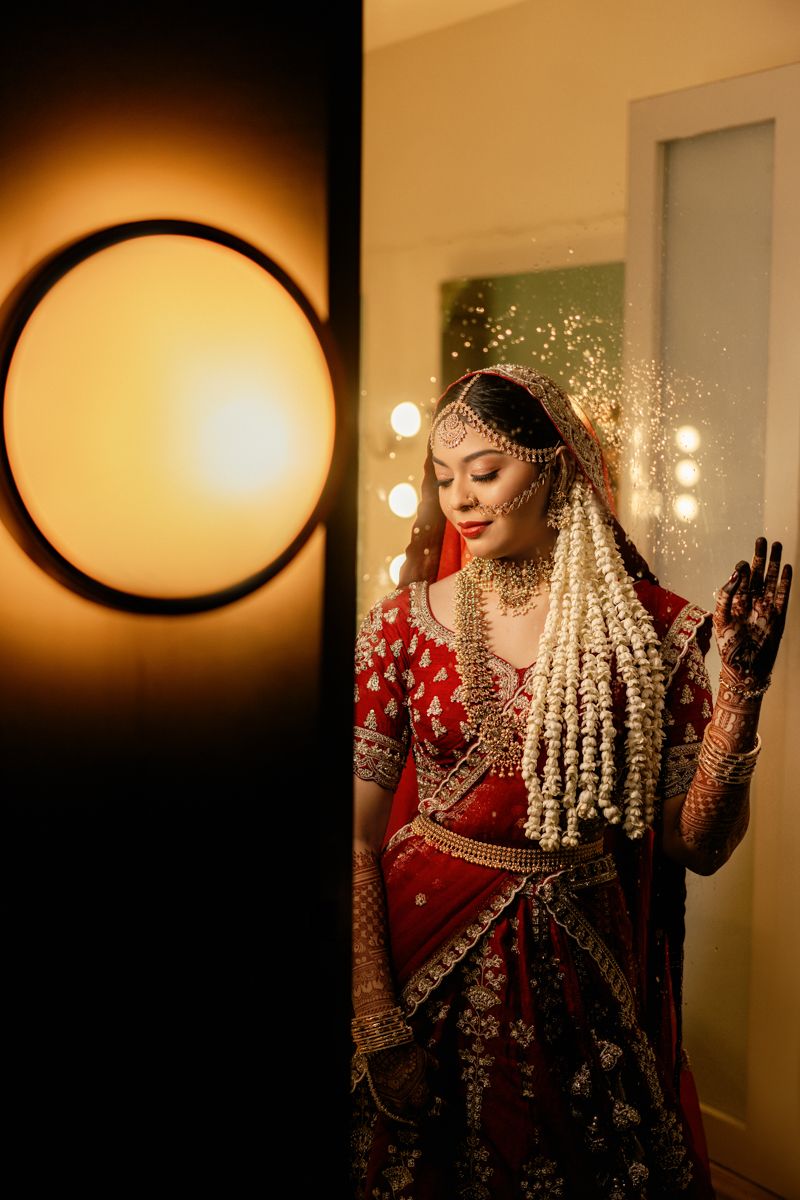 A bride in traditional South Asian wedding attire poses gracefully with henna-adorned hands in warm lighting.
