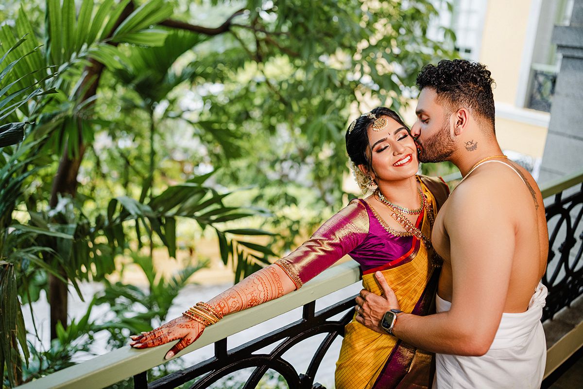 A couple sharing a tender moment on a balcony surrounded by lush tropical plants and greenery.