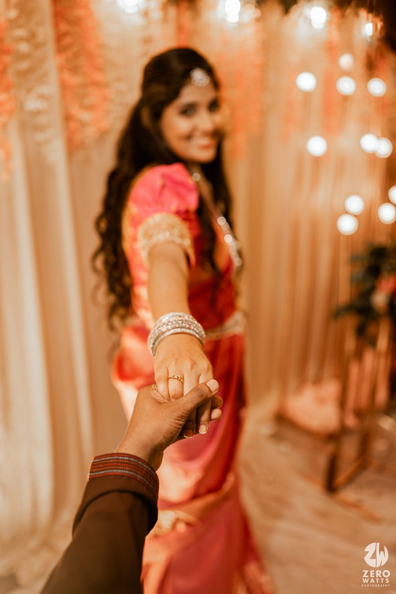 A beautifully decorated engagement photo showing hands clasped together against a backdrop of warm lighting and curtains.