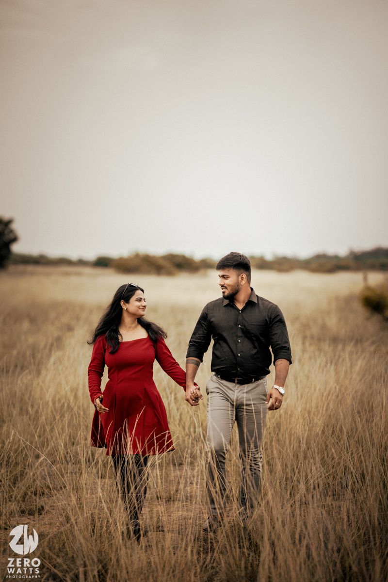 Couple walking hand in hand through a golden grass field at sunset.