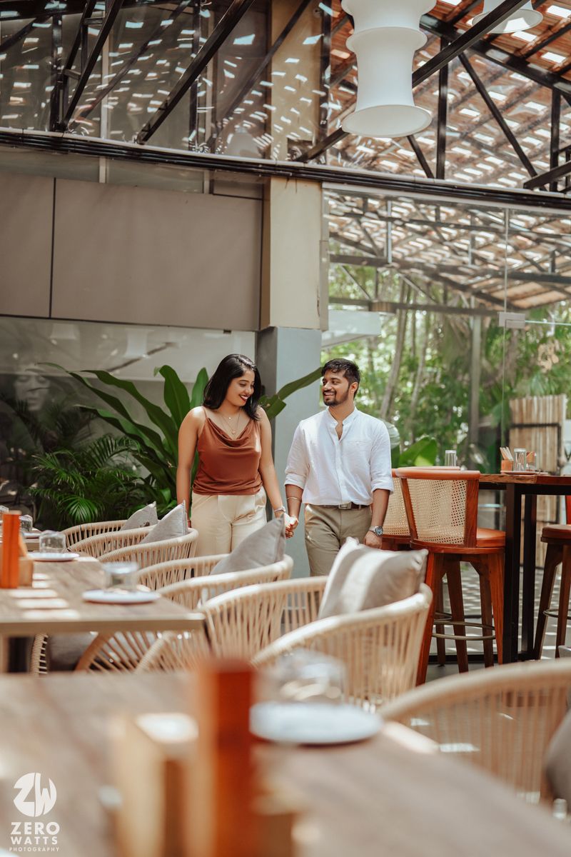A couple sharing a casual moment in a modern restaurant with natural lighting and tropical plants.