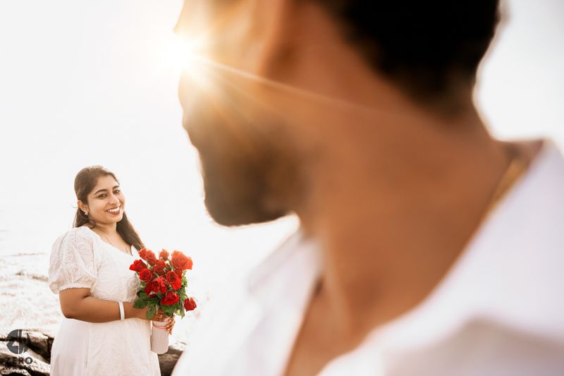 An intimate beachside moment captured with soft lighting and red roses as props.