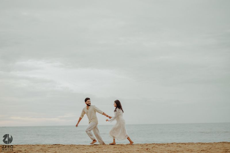 A couple holding hands while running on a serene beach during overcast weather.